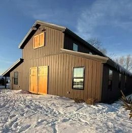 Brown barn-style building with double doors and a window in a snowy landscape at sunset