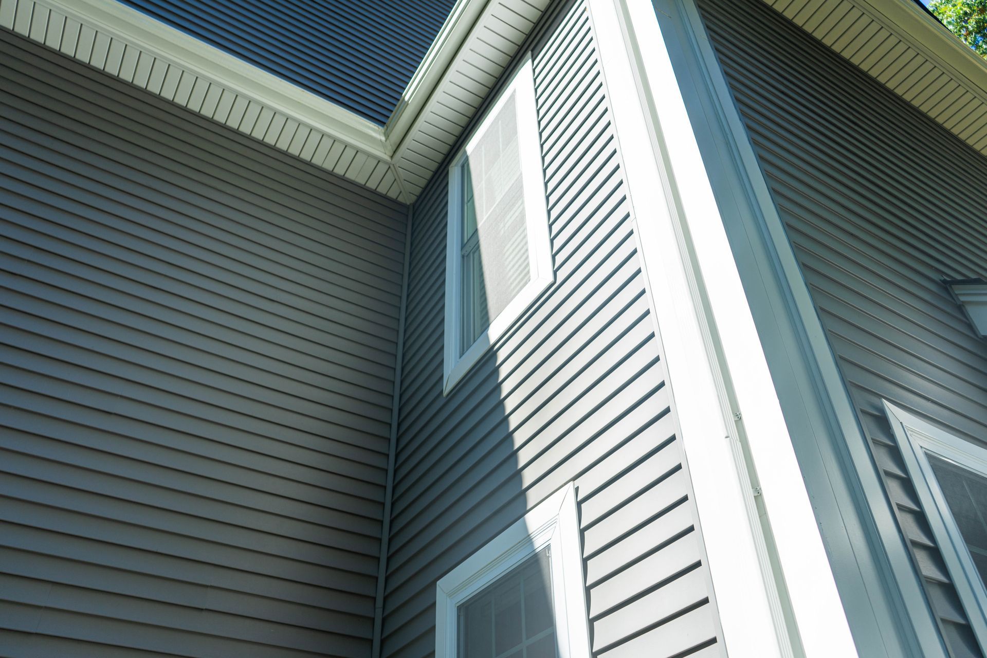 Exterior corner of a gray house with white trim and two windows, viewed upward from below