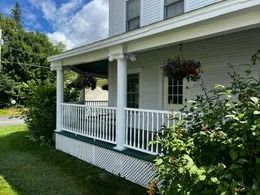 White house porch with railing, hanging flower baskets, and green lawn on a sunny day