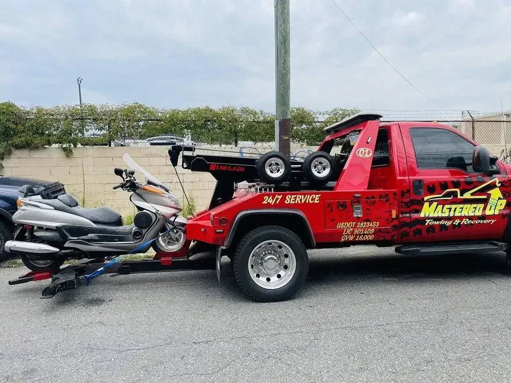 Red tow truck hauling two jet skis on a trailer in a parking lot