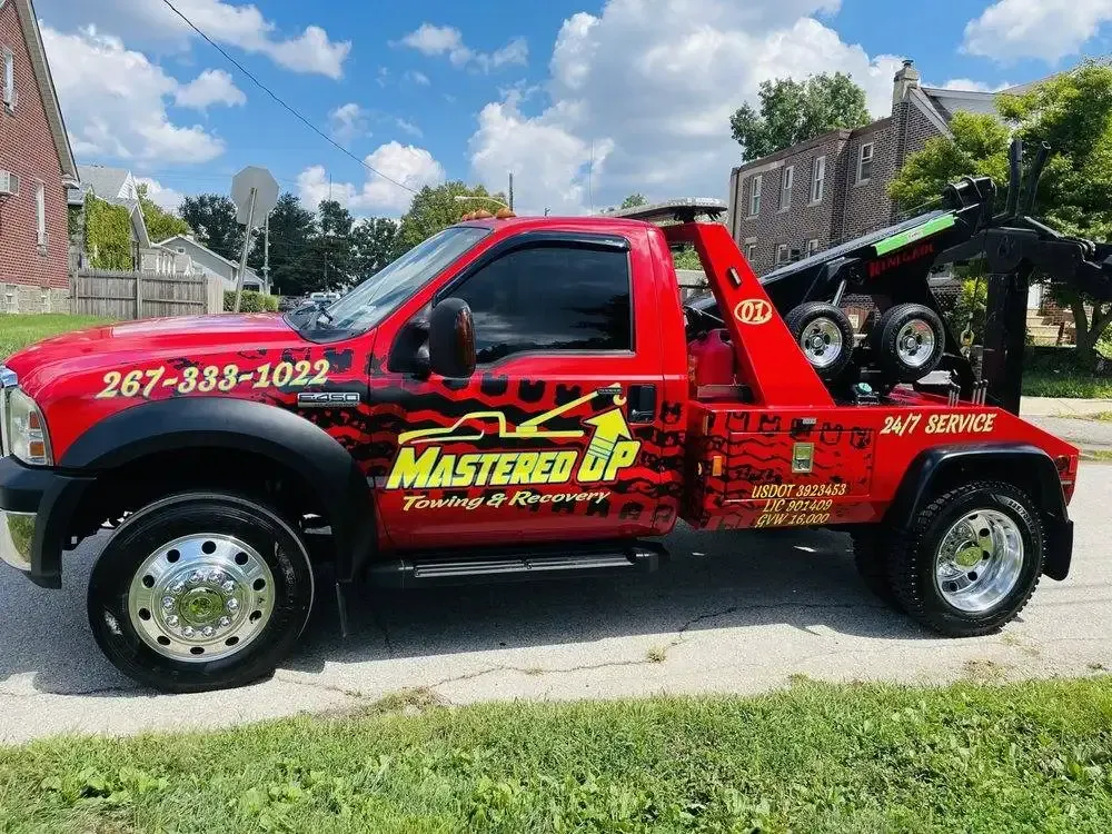 Red and black Master Lube tow truck parked on a suburban street under a blue sky