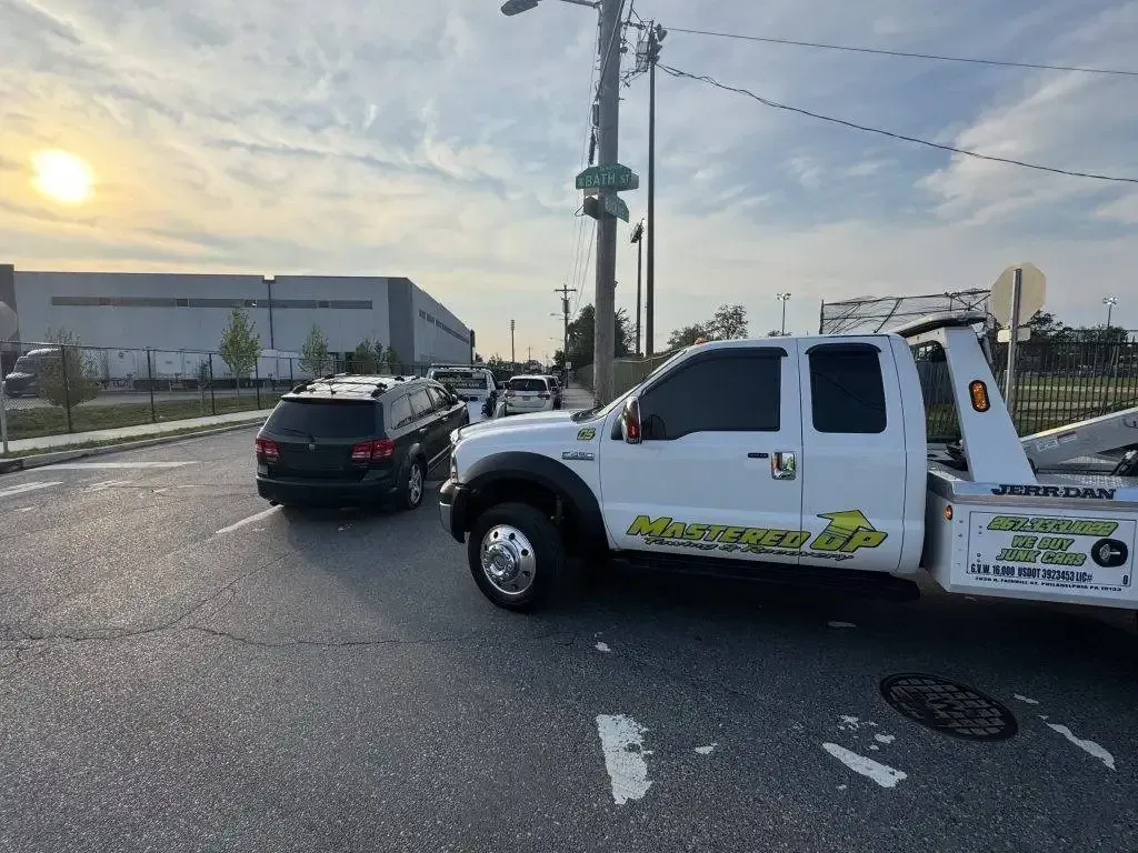 Tow truck blocking a black SUV at an intersection near an industrial building at sunset