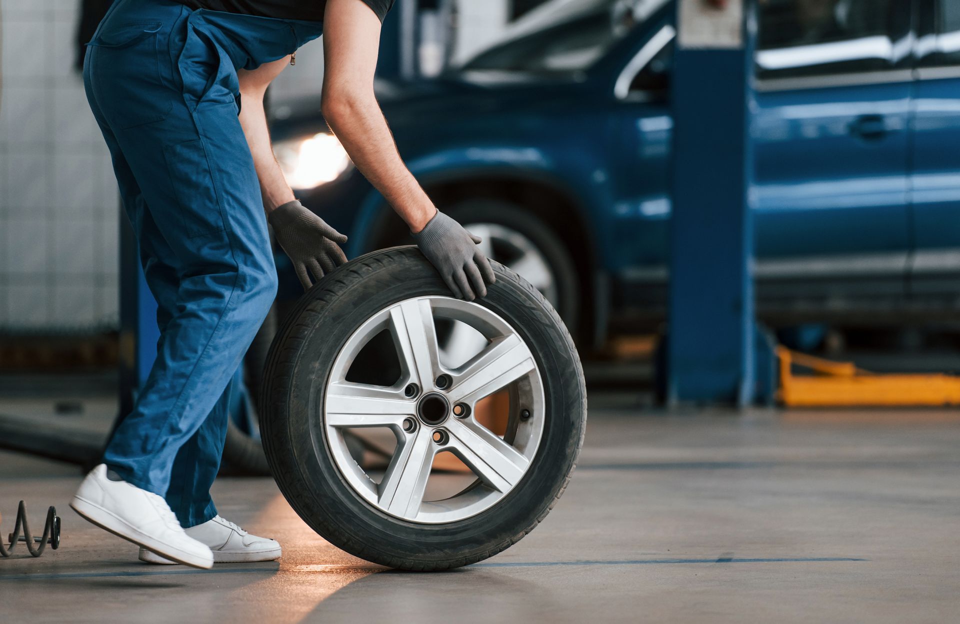Mechanic rolling a tire to a car in an auto repair shop.