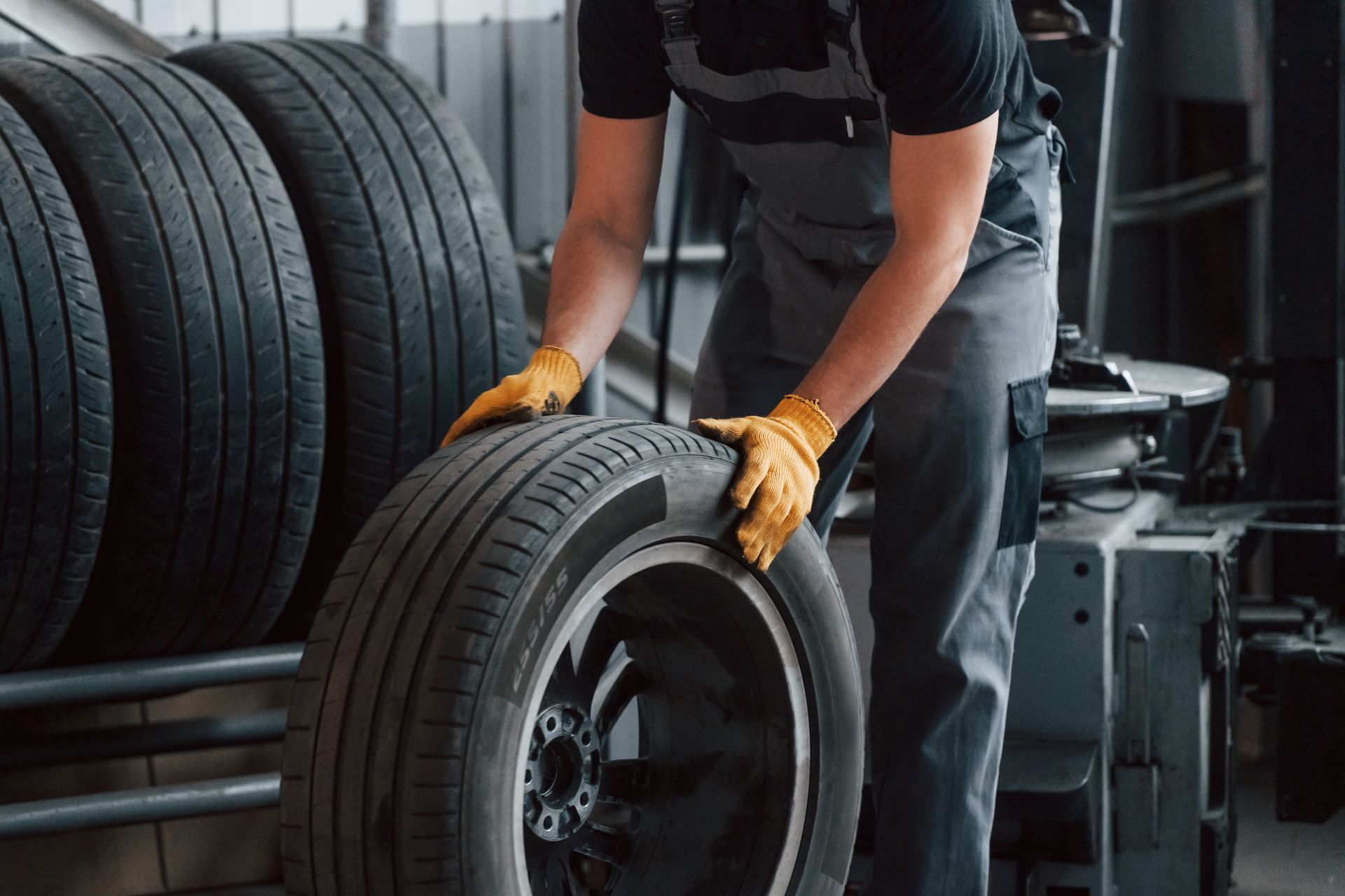 Worker in gloves lifting a car tire in an auto shop with stacked tires in the background