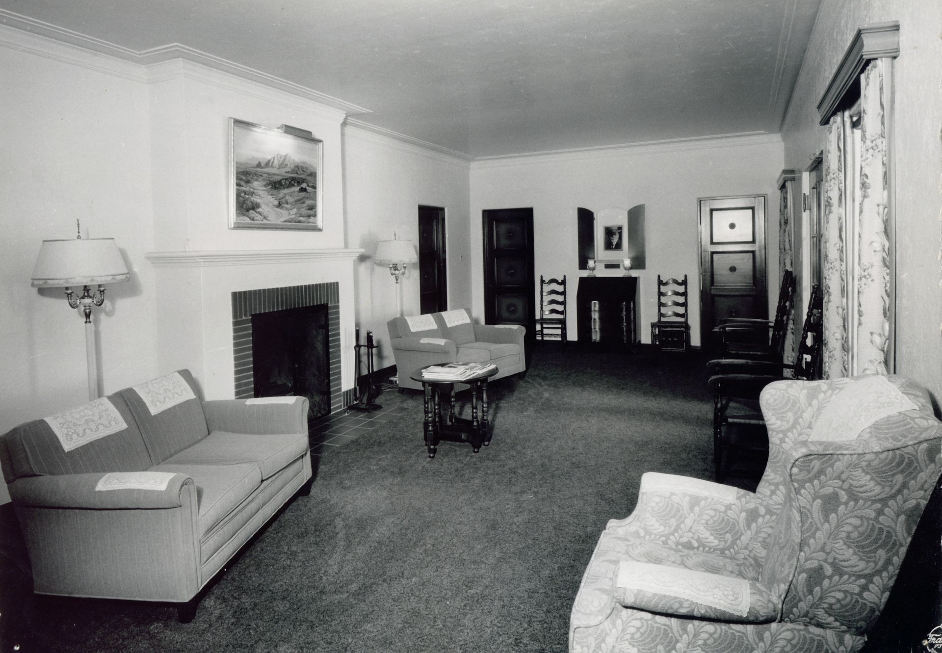 Black-and-white living room with sofas, fireplace, chairs, and a piano in the background