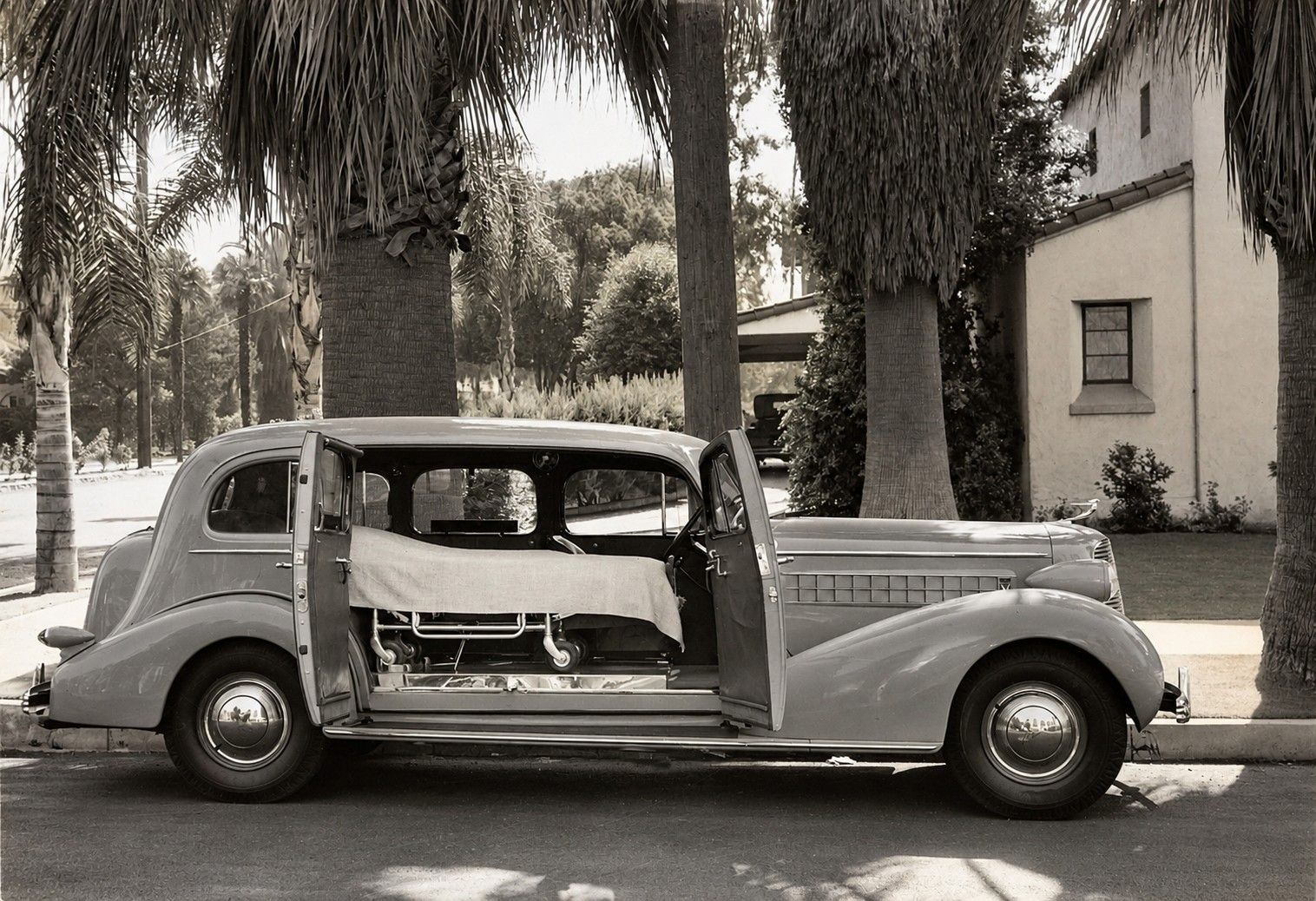 Vintage car parked under palm trees on a sunny street, seen in side view with its interior exposed.