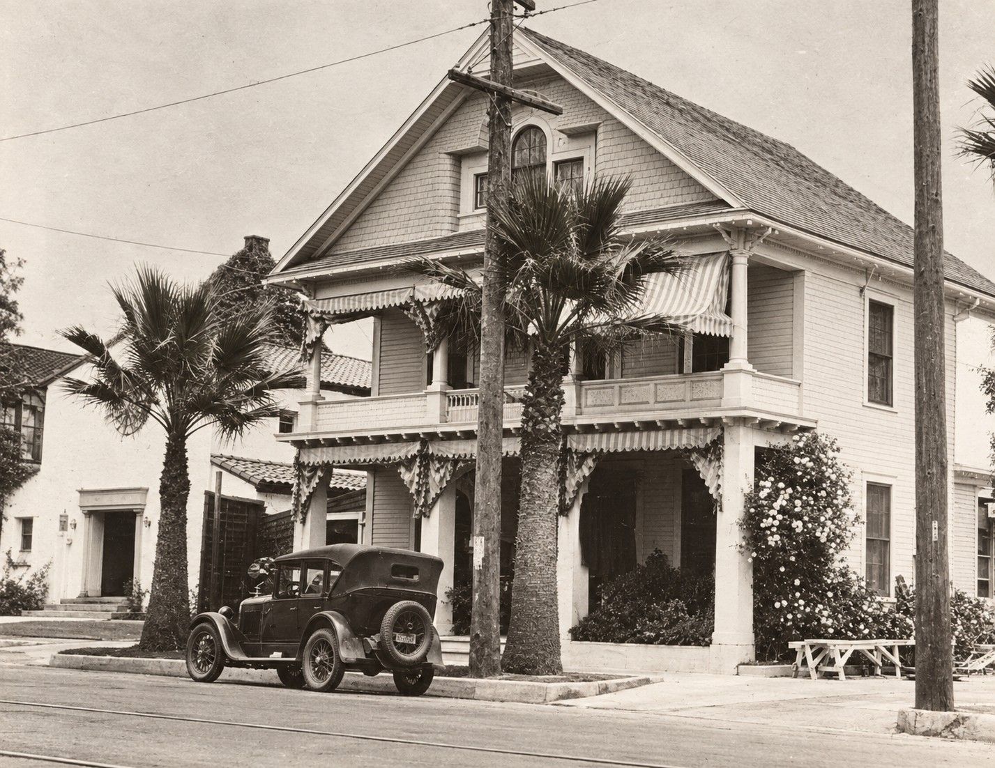 Vintage house with palm trees and an old car parked in front.