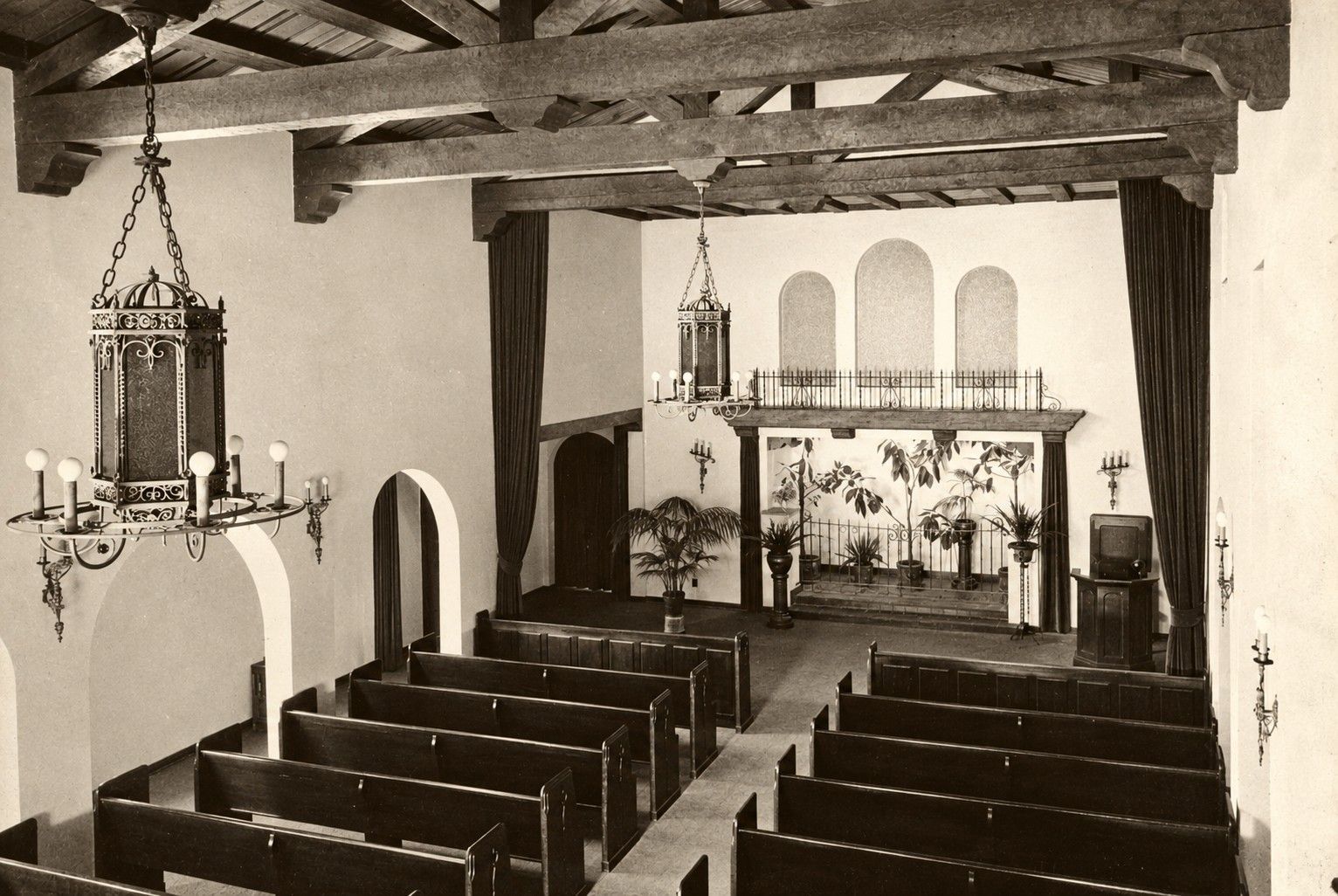 Interior of a small chapel with wooden pews, exposed beams, a pulpit, and an altar at the far end.