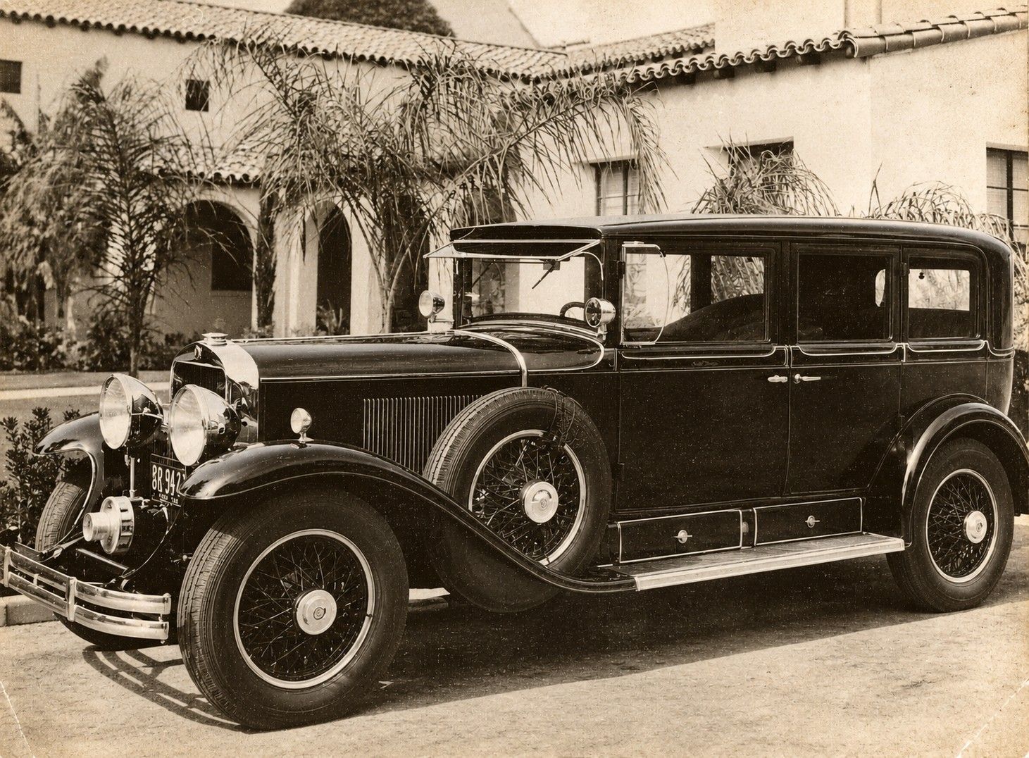 Vintage black luxury car parked in front of a stucco building with arched doorways
