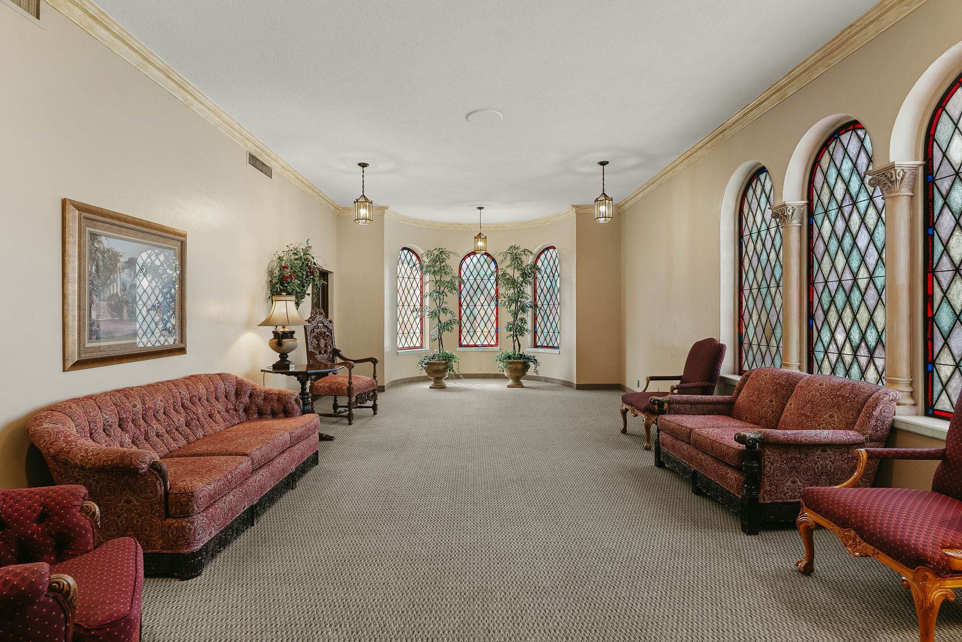Bright waiting room with patterned sofas, carpet, and arched stained-glass windows