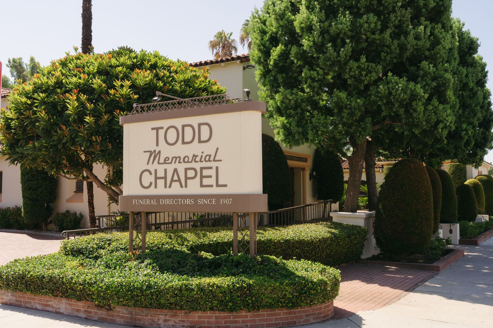 Todd Memorial Chapel sign amid landscaped shrubs and trees outside a beige building