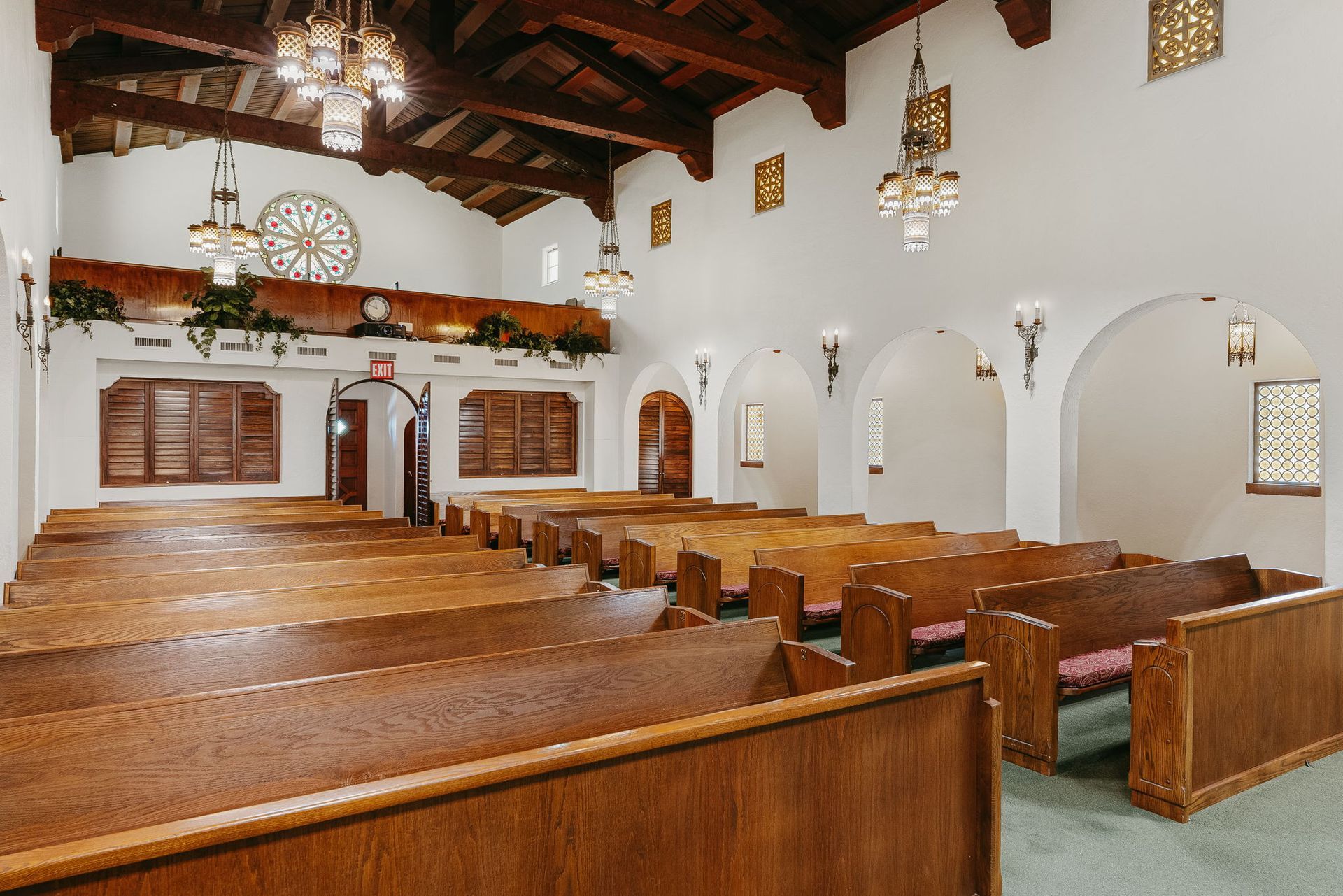 Empty church sanctuary with wooden pews, chandelier lights, and white arched walls