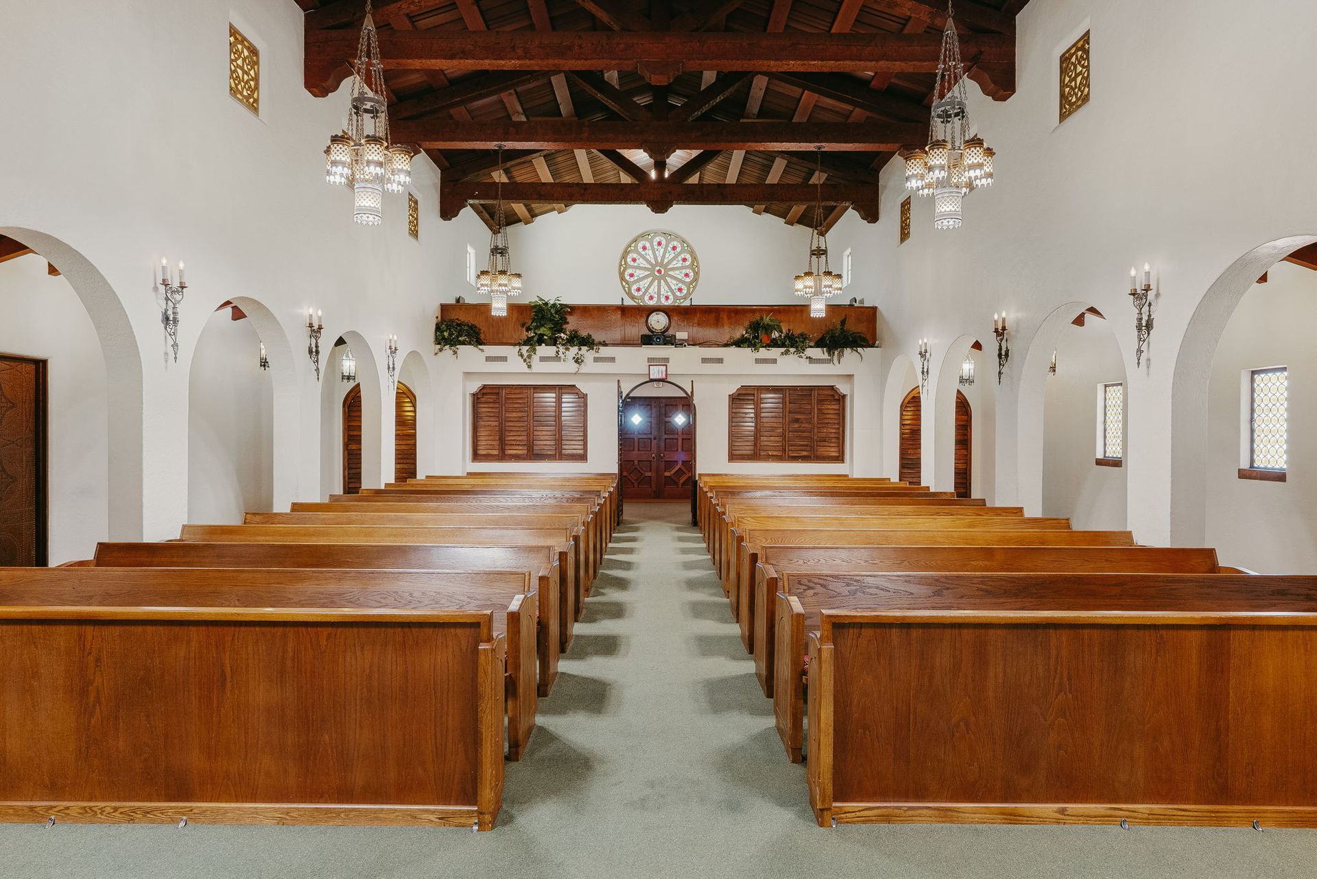 Empty church interior with wooden pews, white walls, and a vaulted timber ceiling, viewed down the center aisle