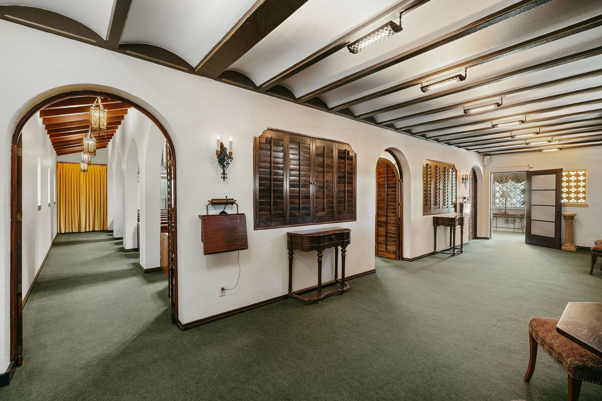Historic interior hallway with arched doorways, green carpet, white walls, and exposed dark ceiling beams