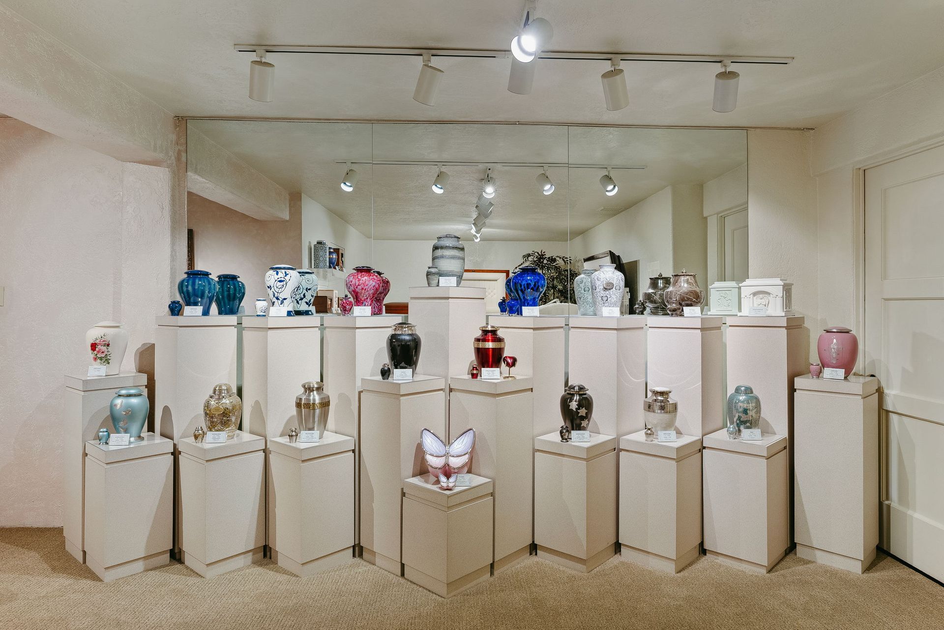 Art gallery display of small sculptures and decorative objects on white pedestals in a bright room