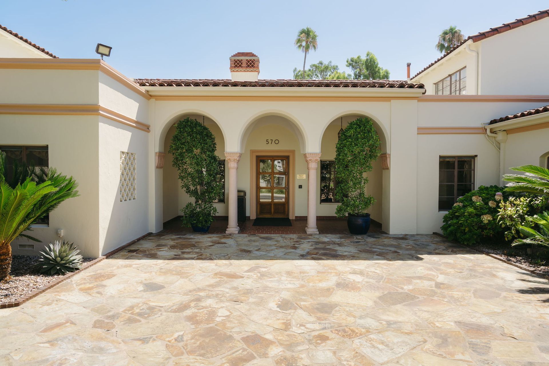 Mediterranean-style house entrance with arched columns, potted plants, and stone courtyard