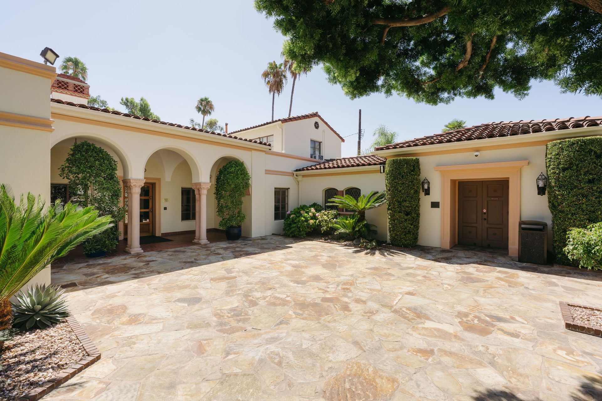 Sunlit Spanish-style courtyard with arched colonnade, terracotta roof, and stone paving