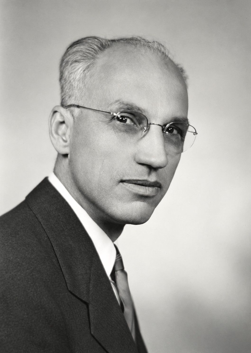 Black-and-white portrait of a man in a suit and glasses, facing slightly left.