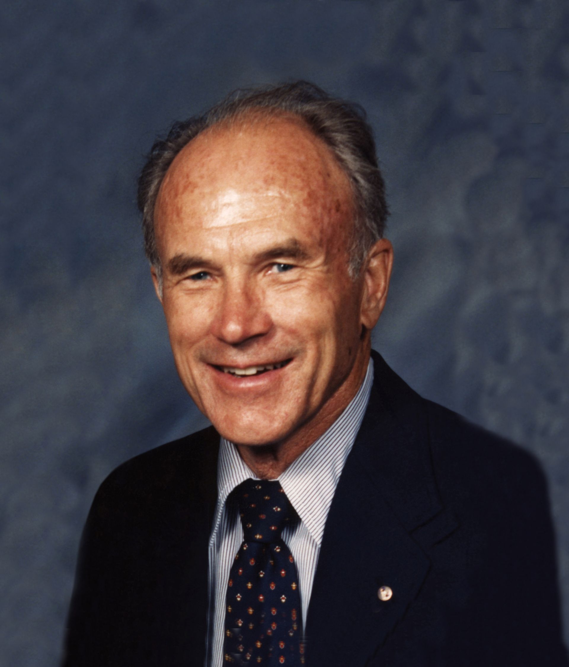 Smiling man in a dark suit and tie against a blue studio backdrop