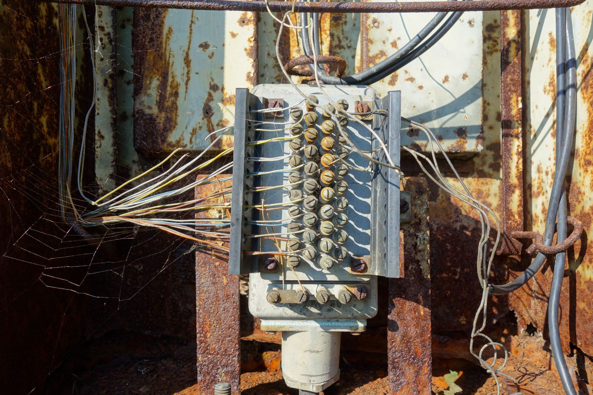 Weathered industrial terminal block with connected wires mounted against a rusted metal wall. Weathered industrial terminal block with connected wires mounted against a rusted metal wall.