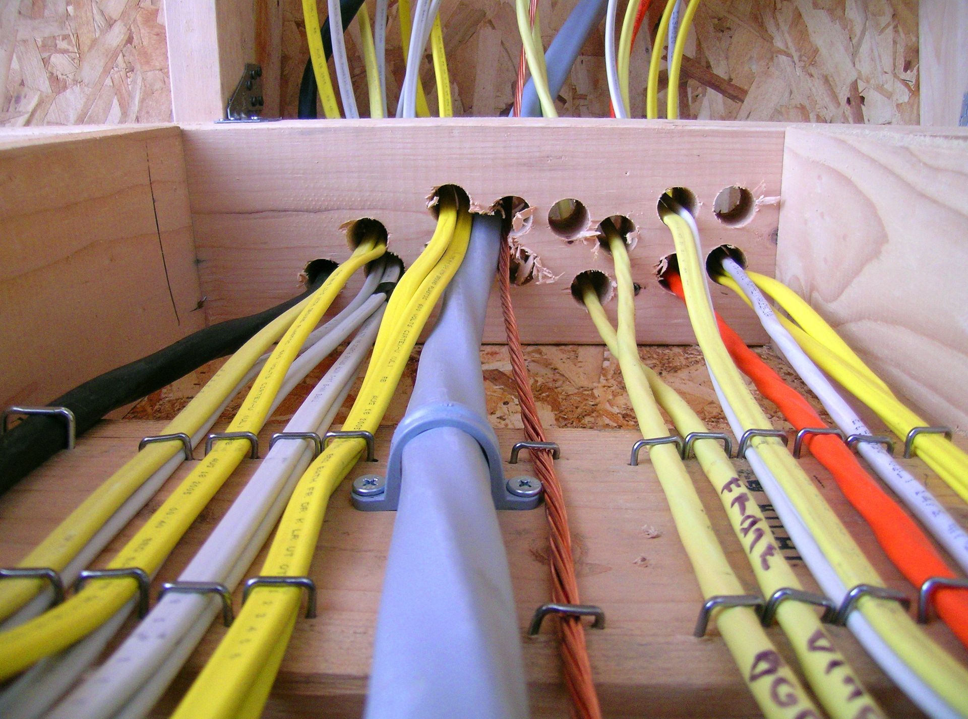 Electrical wires of various colors pass through a wooden frame and are secured with staples and a plastic clamp. Electrical wires of various colors pass through a wooden frame and are secured with staples and a plastic clamp.