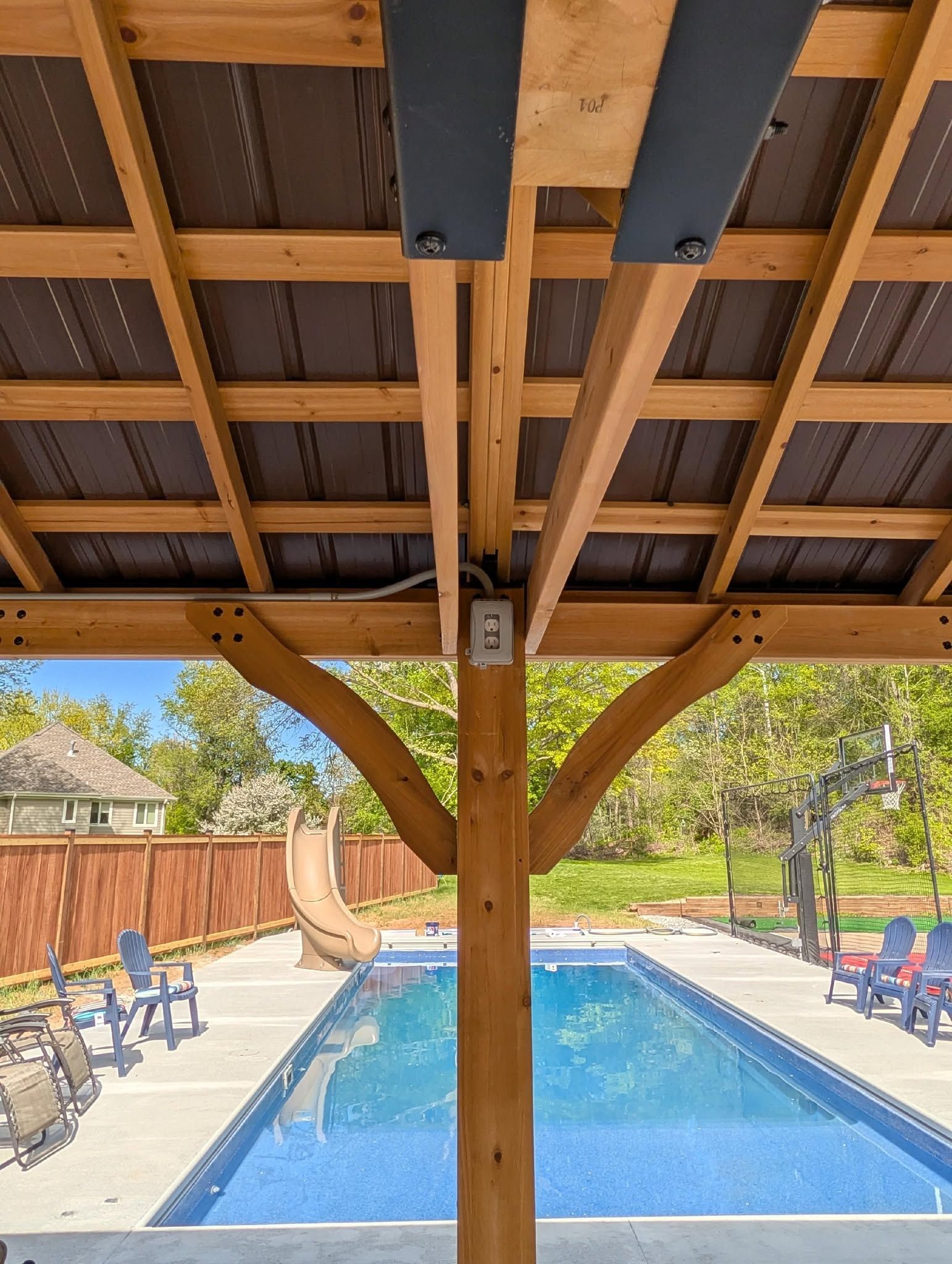 Covered swimming pool with blue water, lounge chairs, and wooden beams overhead in a backyard setting Covered swimming pool with blue water, lounge chairs, and wooden beams overhead in a backyard setting