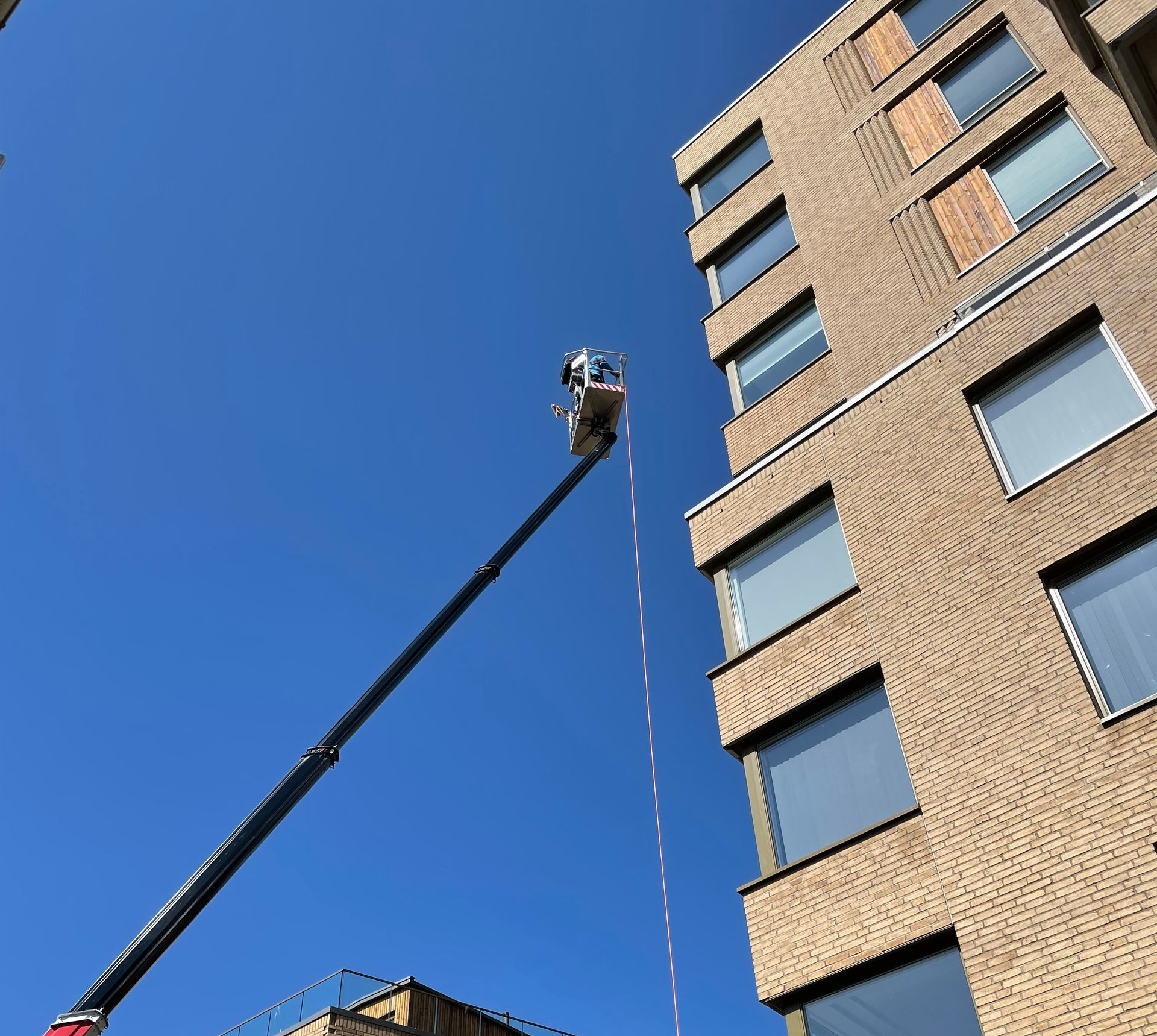 En person rappellerer ned utsiden av en moderne murbygning i flere etasjer med glassvinduer mot en klar blå himmel.