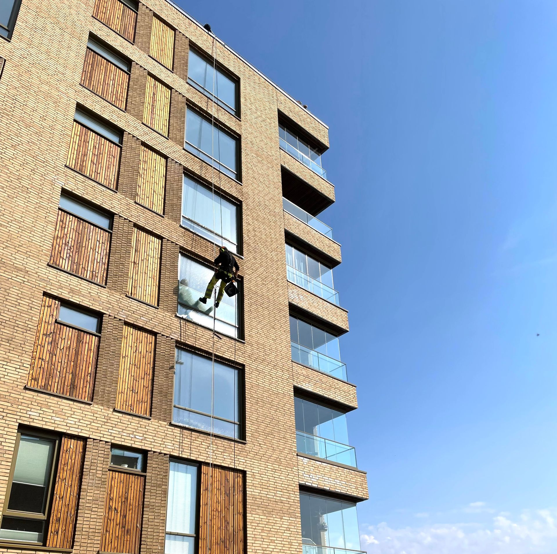 En person rappellerer ned utsiden av en moderne murbygning i flere etasjer med glassvinduer mot en klar blå himmel.