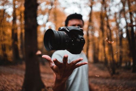 A man is holding a camera in his hand in the woods.