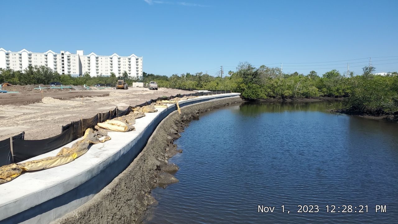 Coastal path beside calm blue water, with apartment buildings and mangroves in the background.