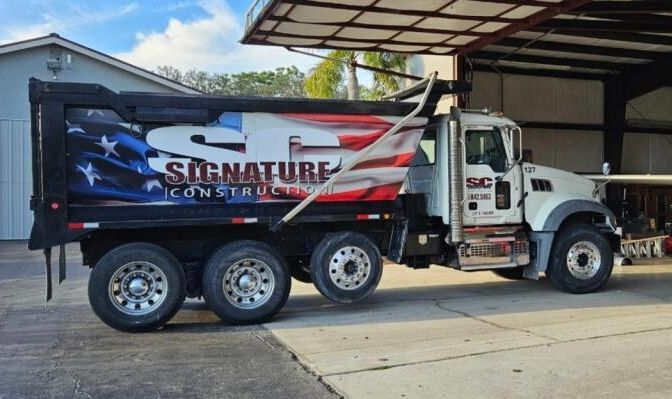 White dump truck with Signature logo parked under a carport.
