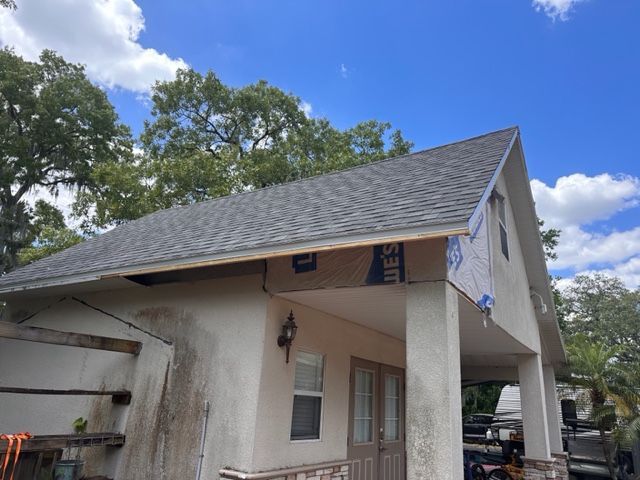 Partially damaged house roof with exposed fascia and loose siding under a blue sky