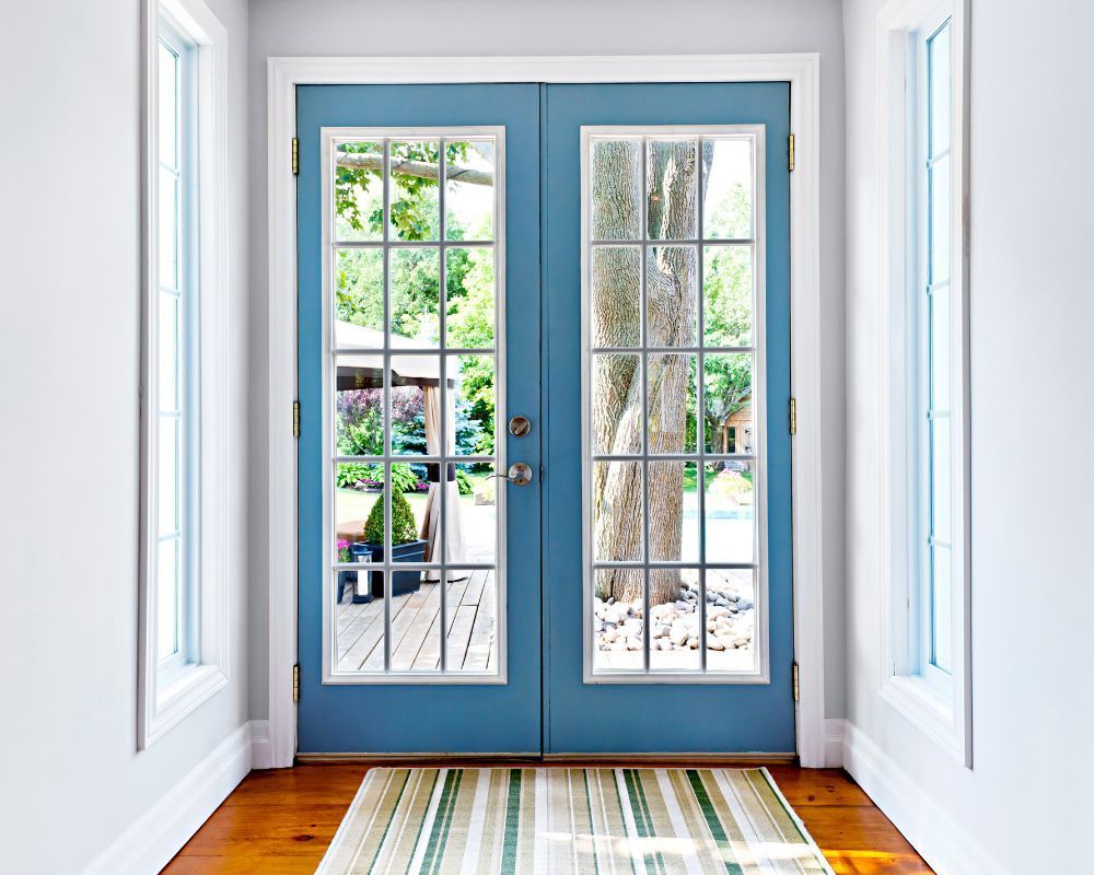 Blue double French doors in a bright entryway, opening to a patio and garden.