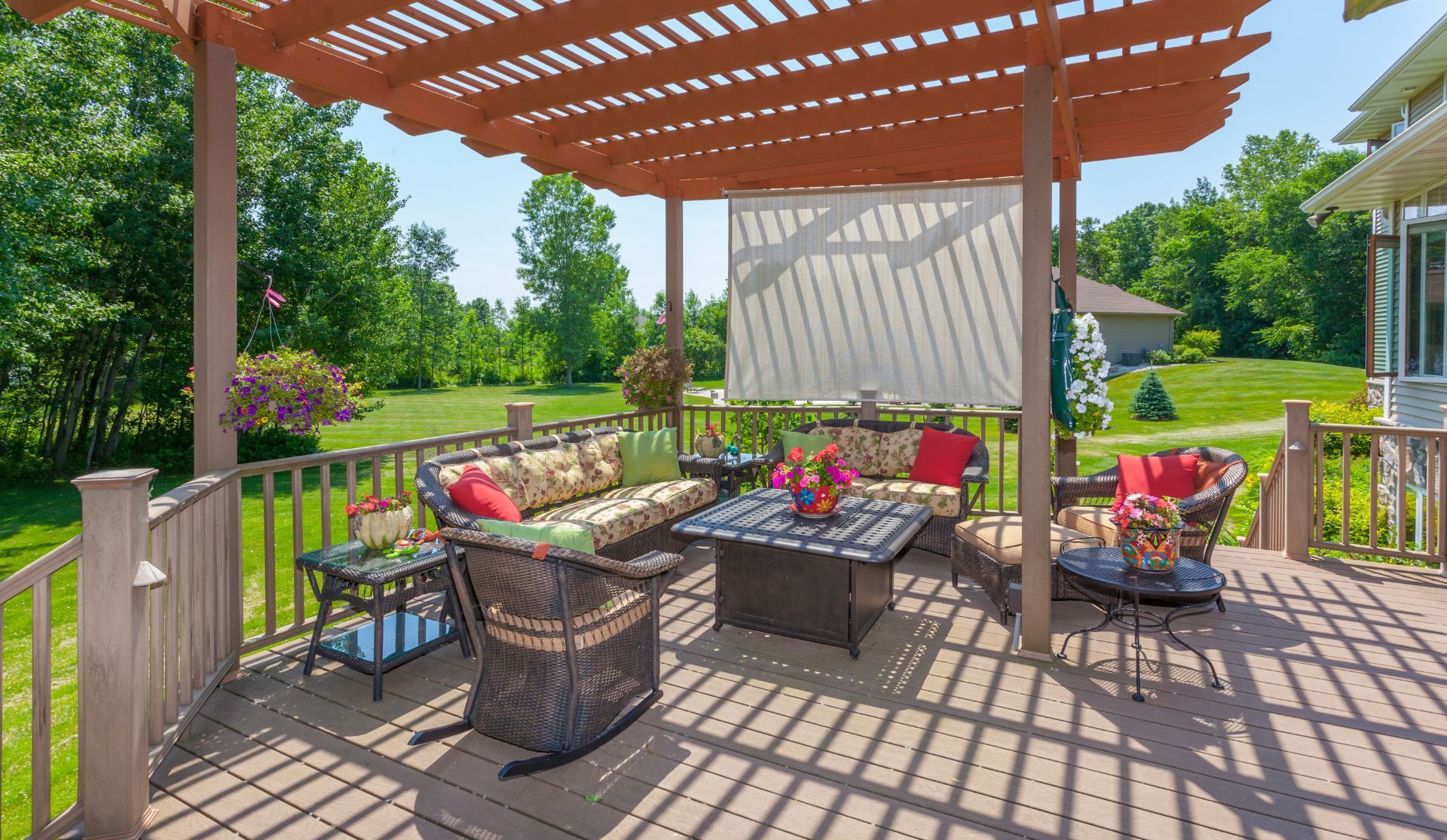 Patio pergola with wicker seating, flower planters, and a fire table on a sunny deck