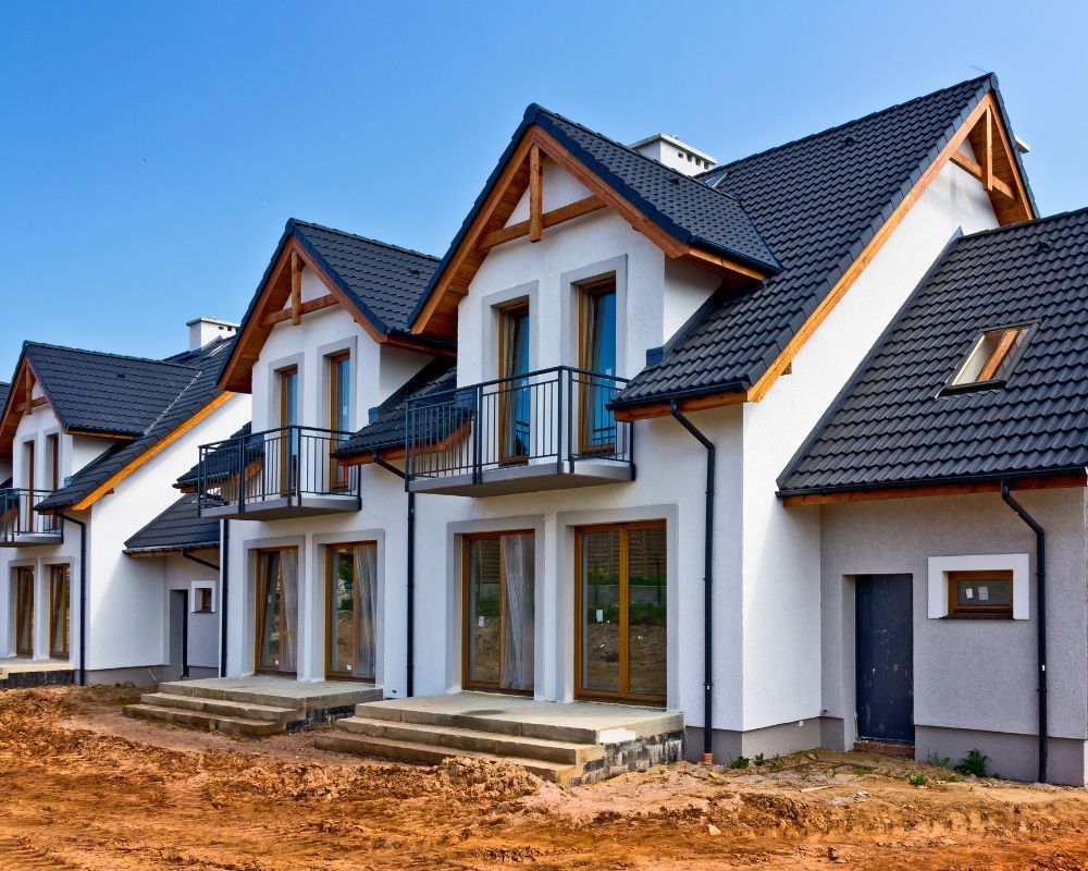 Row of modern white houses with dark roofs and small balconies under construction