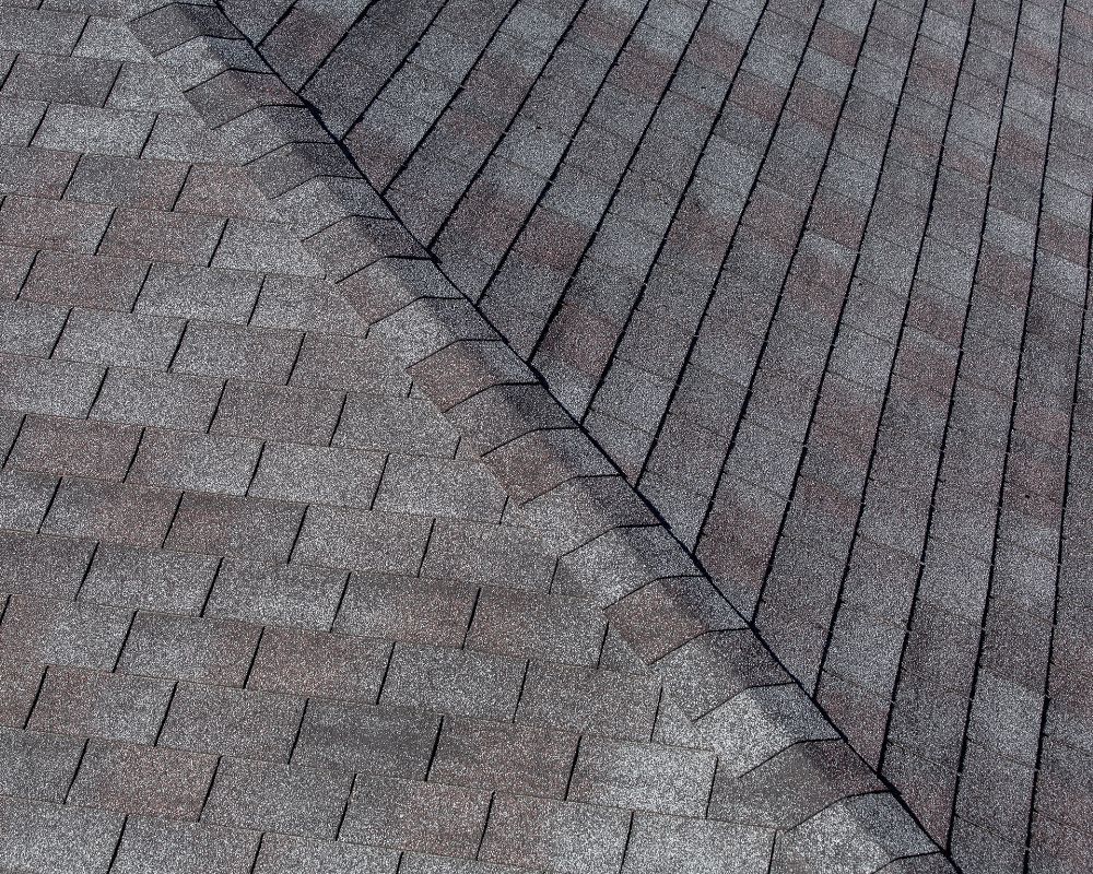 Close-up of gray asphalt roof shingles with a diagonal seam between two roof sections