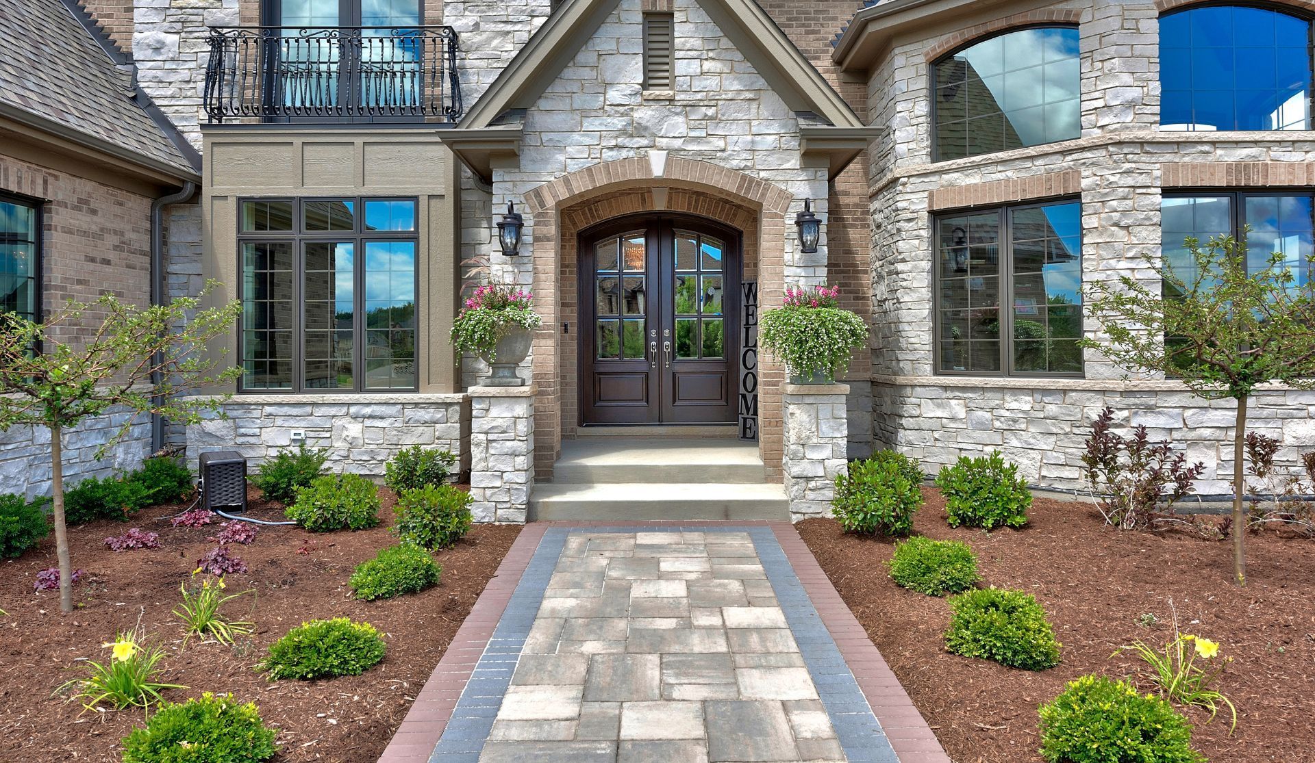 Stone townhouse entrance with arched doorway, potted shrubs, and a paved walkway.