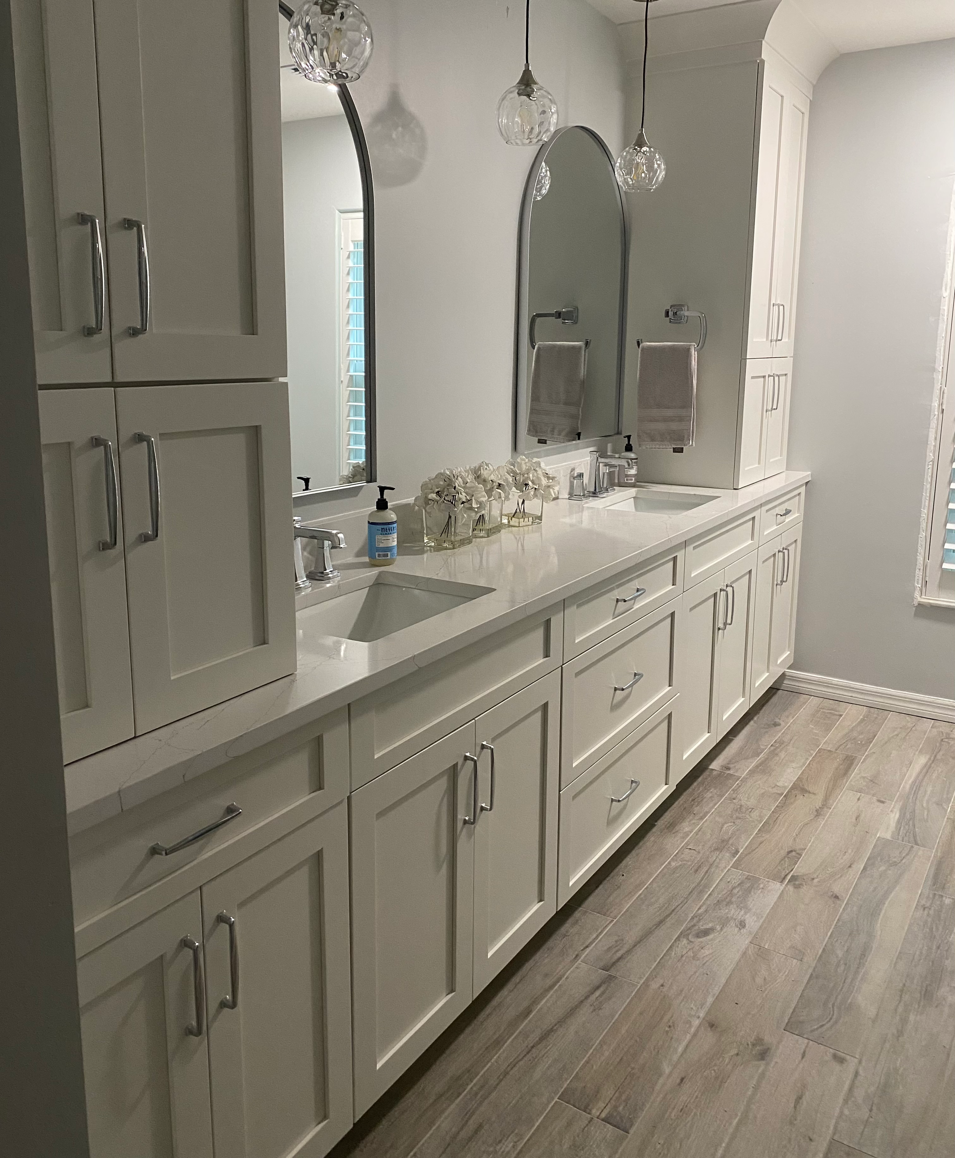 Long white bathroom vanity with double sinks, mirrors, and wood-look flooring.