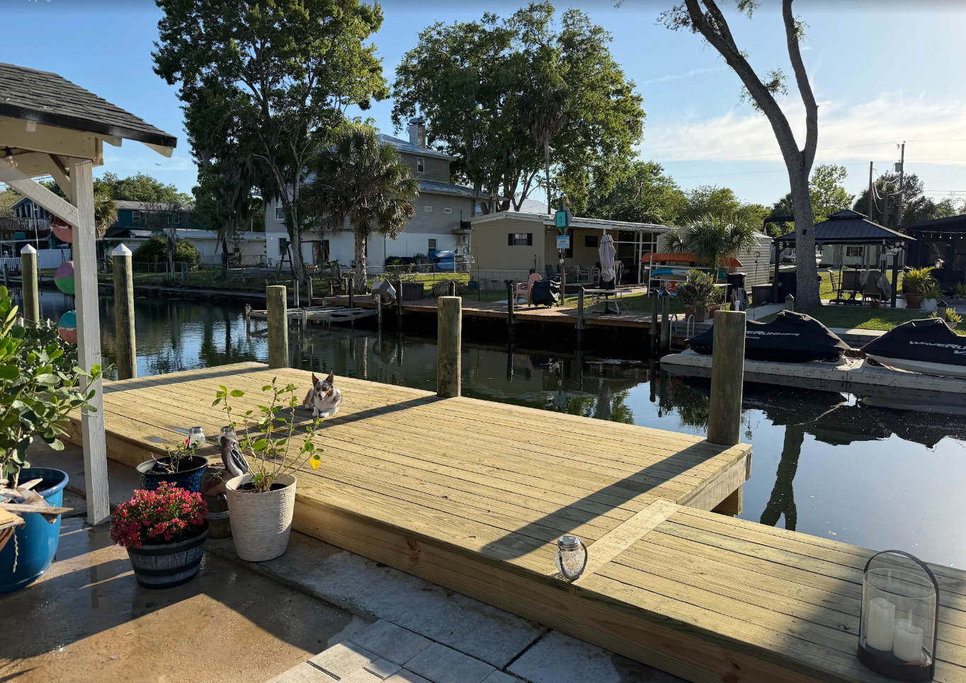 Wooden dock and boat slips on a sunny canal, with potted flowers and waterfront homes nearby