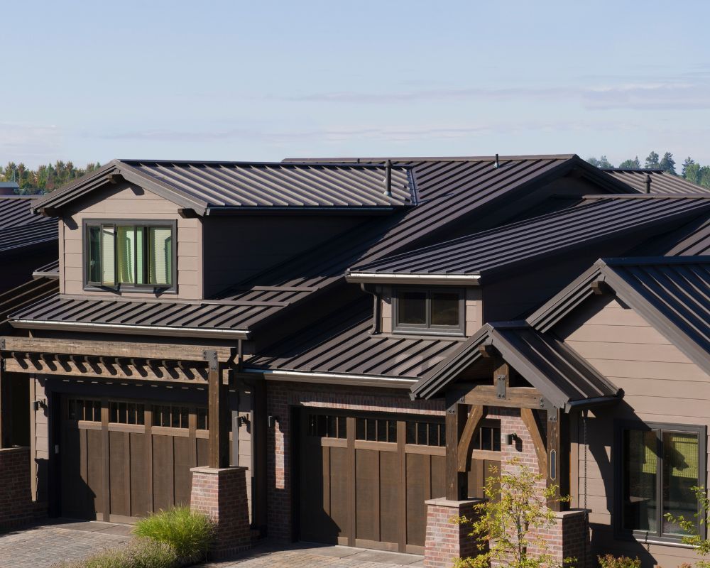 Modern two-story suburban house with dark metal roof and beige siding under a clear sky