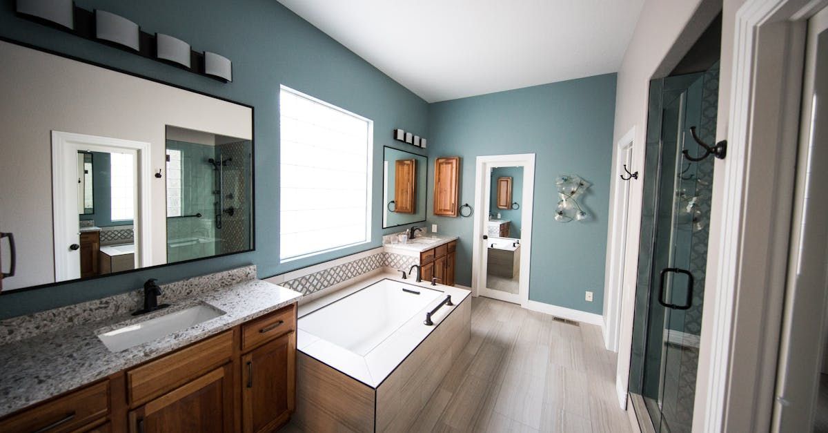Modern bathroom with white tub, wood vanity, teal walls, large window, and glass shower door