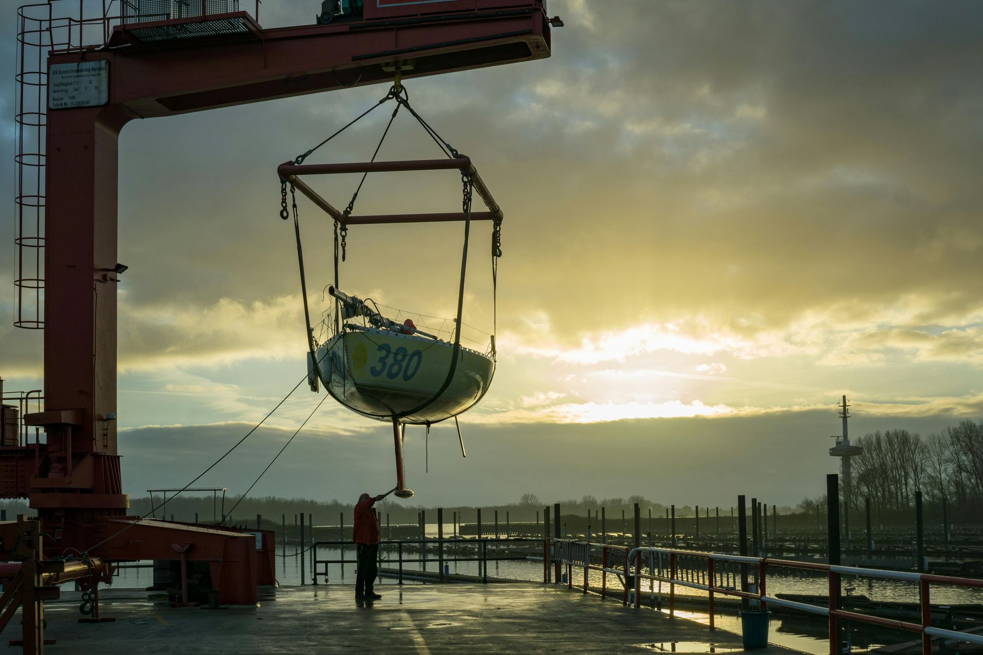 Boat being lifted by crane at sunrise on a wet dock by the water