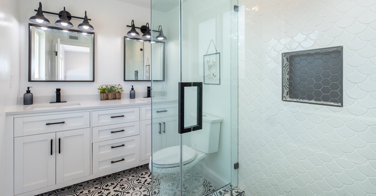 Bright white bathroom with double vanity, mirrors, glass shower, and marble-tile floor.
