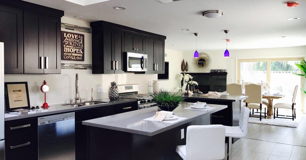 Bright modern kitchen with dark cabinets, island, pendant lights, and dining area by large windows