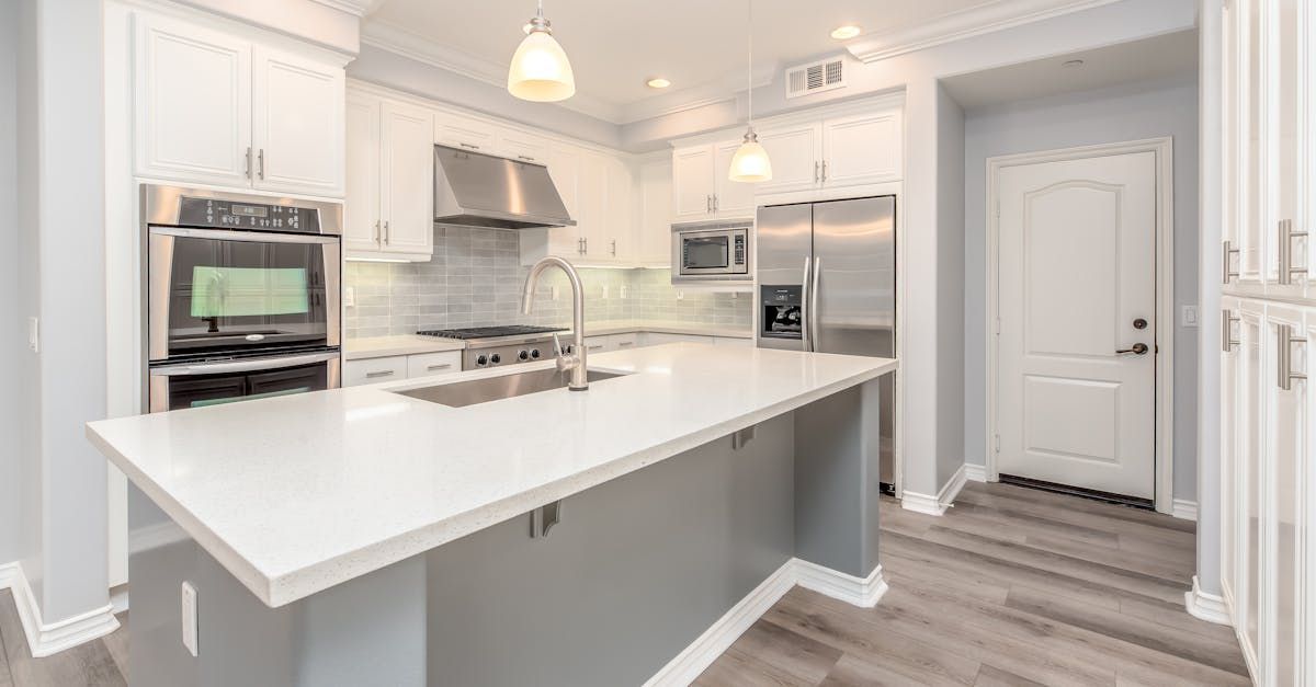 Bright white modern kitchen with large island, stainless appliances, and gray wood-look flooring