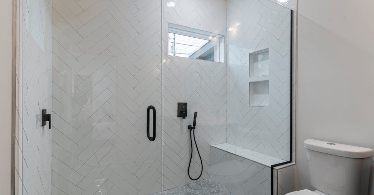 Modern white tiled shower with glass doors, built-in bench, black fixtures, and partial toilet visible