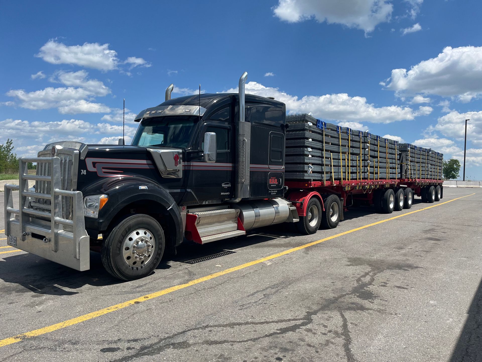 Un semi-remorque noir transportant une longue cargaison de bois sur une autoroute bordée de pins