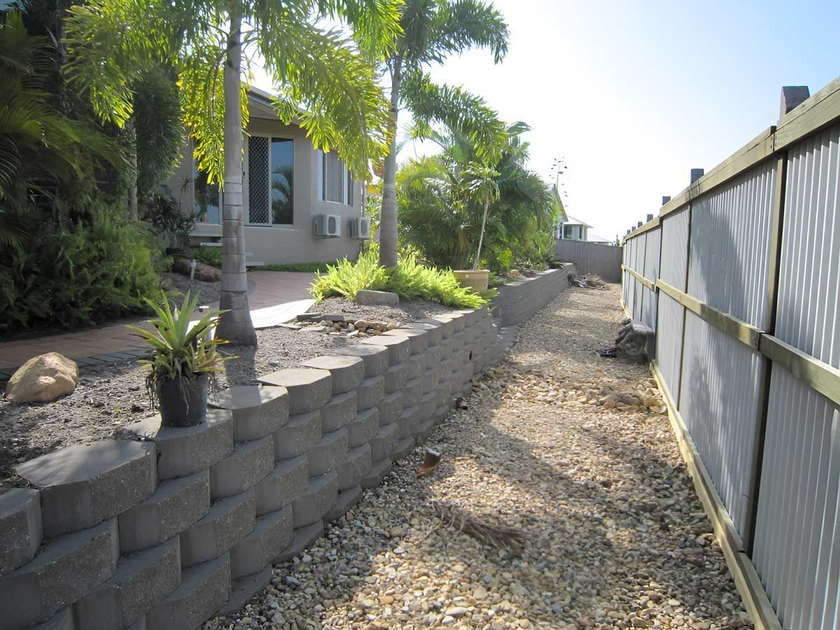 A Garden Brick Wall Along A Dirt Path In Front Of A House — Austen Landscaping & Earthmoving in Deeragun, QLD
