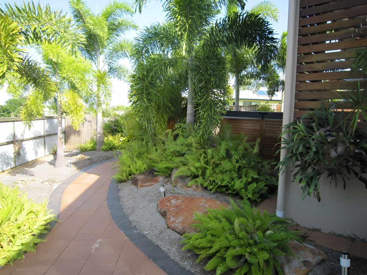 A Lush Green Garden With A Brick Walkway Surrounded By Trees — Austen Landscaping & Earthmoving in Deeragun, QLD