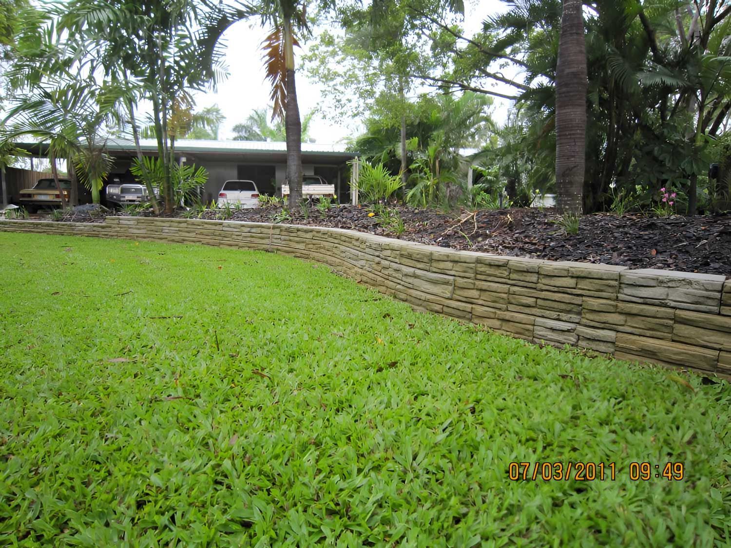 A Vibrant Green Lawn Bordered By A Stone Wall In Front Of A House — Austen Landscaping & Earthmoving in Deeragun, QLD